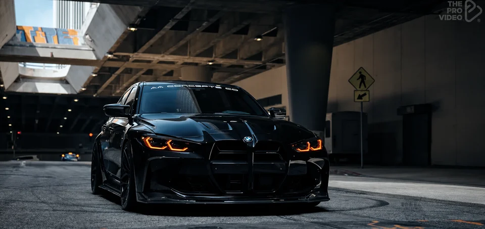 Black BMW with orange headlights beneath a city overpass, from the Balenciaga music video; footage by The Pro Video